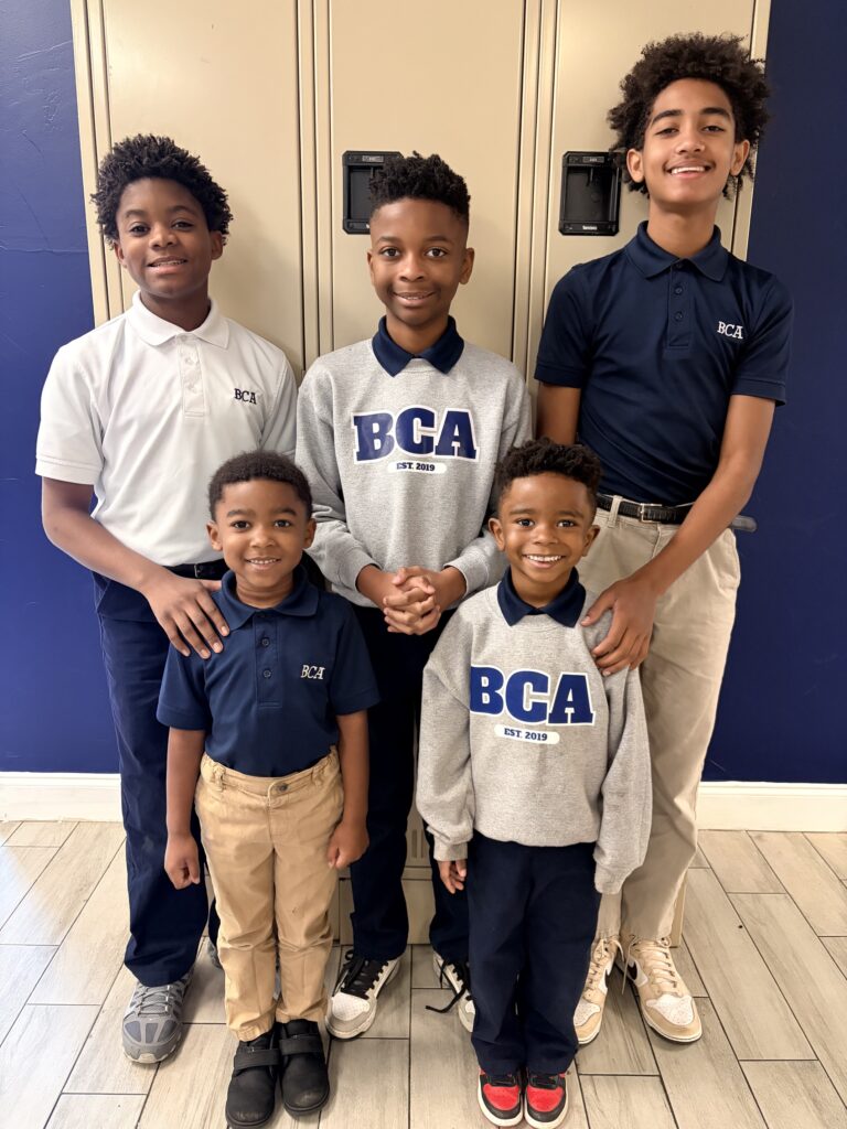 Group of BCA students in school uniforms posing in front of lockers. BCA Est. 2019.